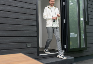 Man komt Sunlodge uit bij Holiday Park 't Rheezerwold, zonnebril op houten tafel op de voorgrond.