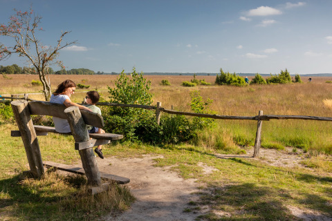 A woman and child sit on a bench at Groeneborg lodge with Hottub, overlooking a scenic open field.