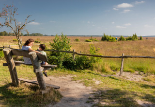 Een vrouw en kind zitten op een bank bij Groeneborg lodge met Hottub, genietend van het landschap.