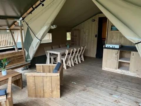 Intérieur d'une tente safari avec meubles en bois, table à manger, coin salon et kitchenette.