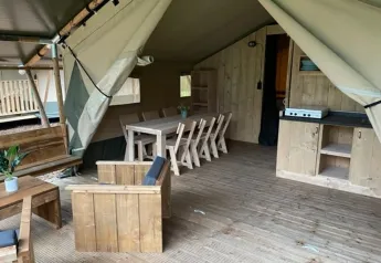 Interno di tenda safari con mobili in legno, tavolo da pranzo, area salotto e cucina compatta.