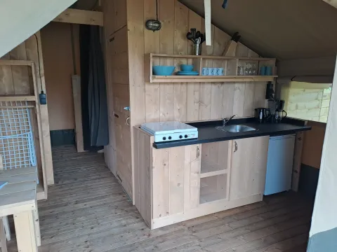 Coin cuisine dans une tente safari avec intérieur en bois et installations sanitaires au Camping de Regenboog en République tchèque.