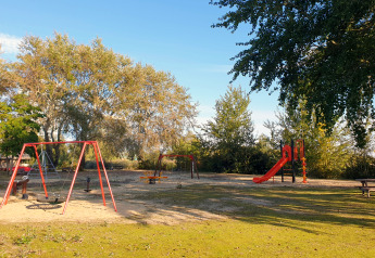 Spielplatz mit Schaukeln, Rutsche und Sitzbank bei einer Glamping-Unterkunft umgeben von Bäumen.