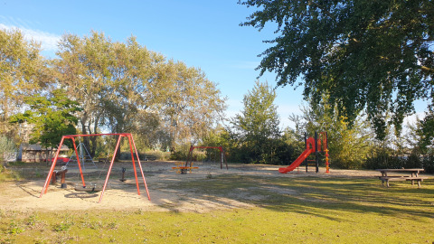 Parque infantil al aire libre en un alojamiento glamping con columpios, tobogán y banco de picnic entre árboles.