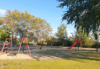 Outdoor playground at a glamping accommodation with swings, slide, and picnic bench surrounded by trees.