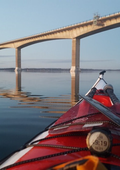 Kayak on calm water near Glyngore Camping, bridge and reflection in water, Central Denmark Region.