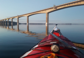 Kayak on calm water near Glyngore Camping, bridge and reflection in water, Central Denmark Region.