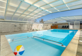 Überdachtes Schwimmbad mit Liegestühlen und buntem Strandball im Glyngore Camping, Dänemark.