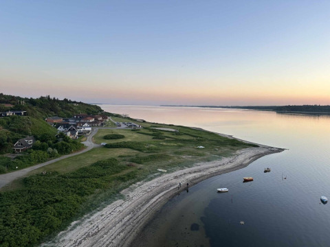 Paysage côtier près de Roslev, Danemark, avec des eaux calmes, des bateaux et des maisons au crépuscule.