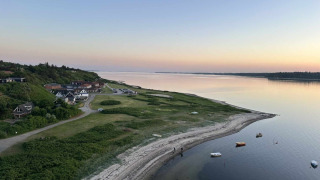 Kystlandskab nær Roslev i Danmark, med rolige vande, både og huse under en klar aftenhimmel.