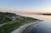 Coastal scenery near Roslev, Denmark, with calm waters, anchored boats, and houses at sunset.