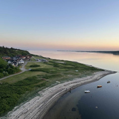 Coastal scenery near Roslev, Denmark, with calm waters, anchored boats, and houses at sunset.