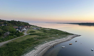 Coastal scenery near Roslev, Denmark, with calm waters, anchored boats, and houses at sunset.