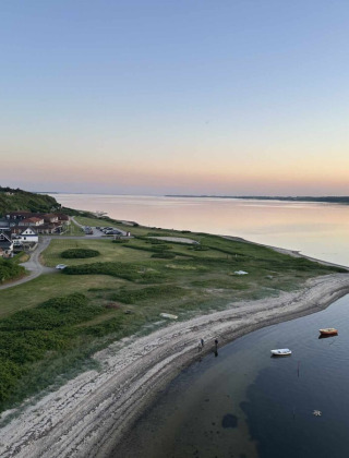 Kystlandskab nær Roslev i Danmark, med rolige vande, både og huse under en klar aftenhimmel.