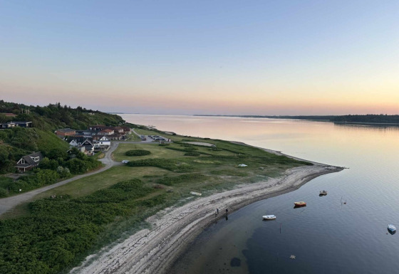 Coastal scenery near Roslev, Denmark, with calm waters, anchored boats, and houses at sunset.