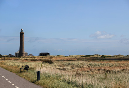 Landscape near Roslev, Denmark with a tall lighthouse, grassy fields, and a bright blue sky.