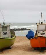 Two fishing boats rest on a sandy beach with rough sea and cloudy sky near Roslev, Denmark.