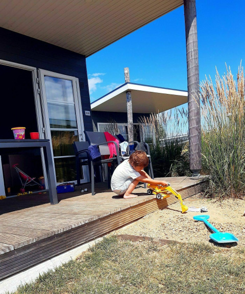 Jonge jongen speelt met graafmachine op houten terras bij vakantiehuisje in Kompas Camping Westende.