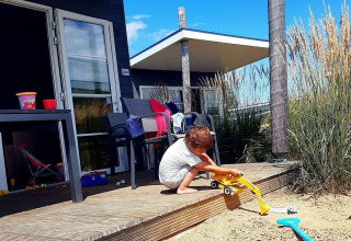Jonge jongen speelt met graafmachine op houten terras bij vakantiehuisje in Kompas Camping Westende.