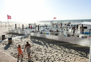 Strandrestaurant met witte omheining en mensen genietend van eten bij Kompas Camping Westende, België.