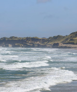 Waves roll onto a sandy beach near Aars, North Jutland, with dunes and a solitary house in the background.