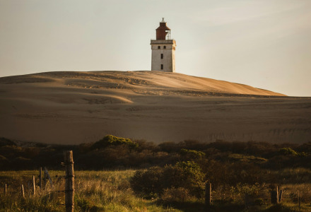 Lighthouse on a sand dune near Aars, North Jutland, Denmark, surrounded by greenery and a winding path at dusk.