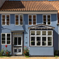 Charming light blue townhouse with red tiled roof and many windows in Aars, North Jutland, Denmark.