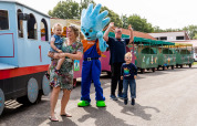Gezin geniet bij een kleurrijk treintje met een vrolijke mascotte op vakantiepark De Tien Heugten.