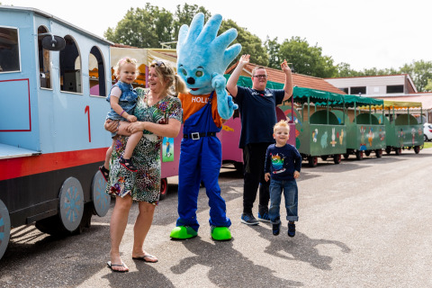 Gezin geniet bij een kleurrijk treintje met een vrolijke mascotte op vakantiepark De Tien Heugten.