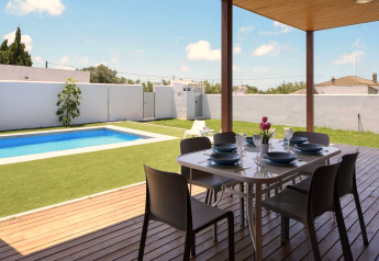 Terrasse bei Casa Toria in Spanien mit Esstisch, Stühlen, Pool und Garten unter blauem Himmel.