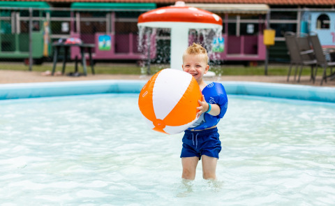 Jonge jongen speelt lachend met een strandbal in een ondiep zwembad bij De Tien Heugten vakantiepark.