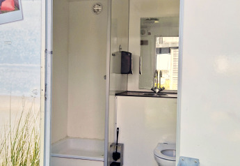 Glampingbadkamer met een douche, toilet en wastafel, gezien via een open deur overdag.