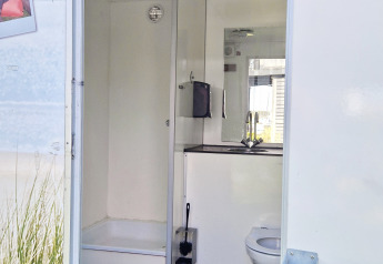 Bagno da glamping con doccia, wc e lavandino, visto attraverso una porta aperta durante il giorno.