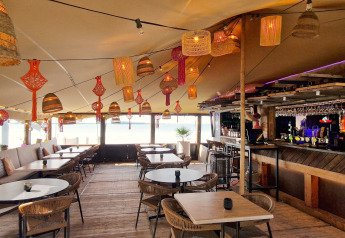 Area lounge accogliente presso una struttura glamping con lampade in vimini, tavoli e un bancone bar.