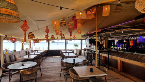 Sfeervolle lounge bij een glampingaccommodatie met rieten lampen, houten tafels en een gezellige bar.