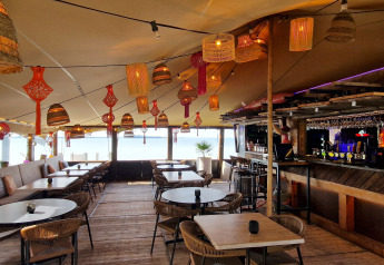 Udendørs loungestemning på et glampingsted med hyggelig belysning, borde, stole og en bar i baggrunden.