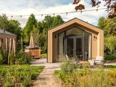 Tiny house moderne en bois avec grandes fenêtres, terrasse, coin salon extérieur et bain à remous au jardin.
