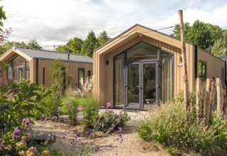 Moderne tiny house 'Tiny Lodge' med boblebad på Veluwepark de Bosgraaf, omringet af grønne planter i Holland.