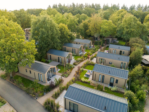 Vue aérienne de tiny houses modernes en rangées avec des jardins et arbres dans un cadre naturel verdoyant.