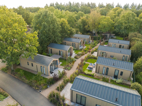 Luftfoto af flere Tiny Lodge hytter med boblebad på Veluwepark de Bosgraaf i Holland omgivet af træer.