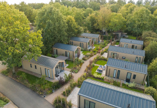 Vista aérea de varias Tiny Lodge con jacuzzi en Veluwepark de Bosgraaf, Países Bajos, rodeadas de árboles.