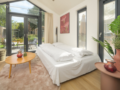 Moderne soveværelse med store vinduer og udsigt til have, indrettet i Tiny Lodge på Veluwepark de Bosgraaf.