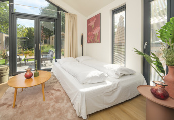 Modernes Schlafzimmer mit großen Fenstern und Gartenausblick im Tiny Lodge im Veluwepark de Bosgraaf.
