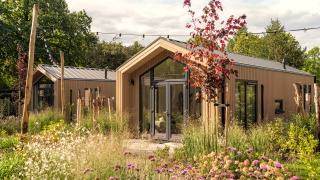 Tiny Lodge : Petite maison moderne en bois, entourée d’un jardin luxuriant et de fleurs sauvages colorées.