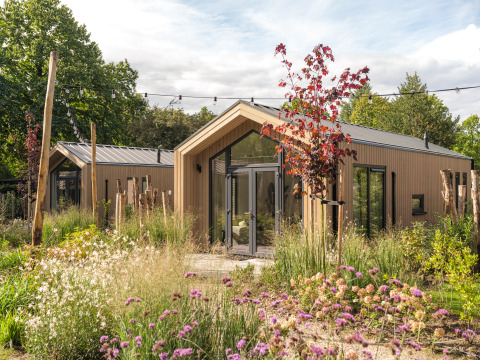 Tiny Lodge : Petite maison moderne en bois, entourée d’un jardin luxuriant et de fleurs sauvages colorées.