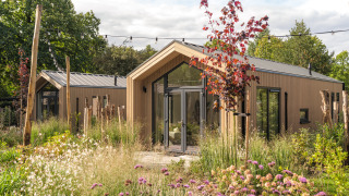 Tiny Lodge : Petite maison moderne en bois, entourée d’un jardin luxuriant et de fleurs sauvages colorées.