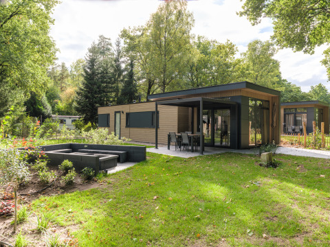 Moderne Cannenburch Deluxe lodge met grote ramen, buitenterras en tuin, omringd door veel groen.