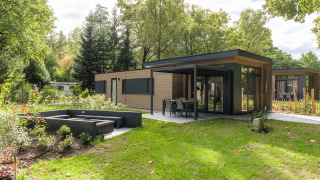 Lodge moderno Cannenburch Deluxe con grandi finestre, terrazza esterna e giardino circondato dal verde.