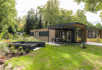 Moderna cabaña Cannenburch Deluxe con terraza, ventanales y jardín, rodeada de árboles y vegetación.
