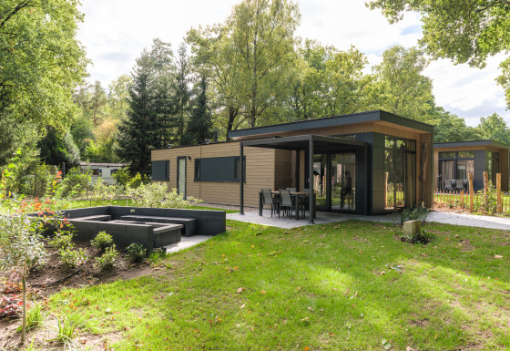 Moderne Cannenburch Deluxe lodge met grote ramen, buitenterras en tuin, omringd door veel groen.